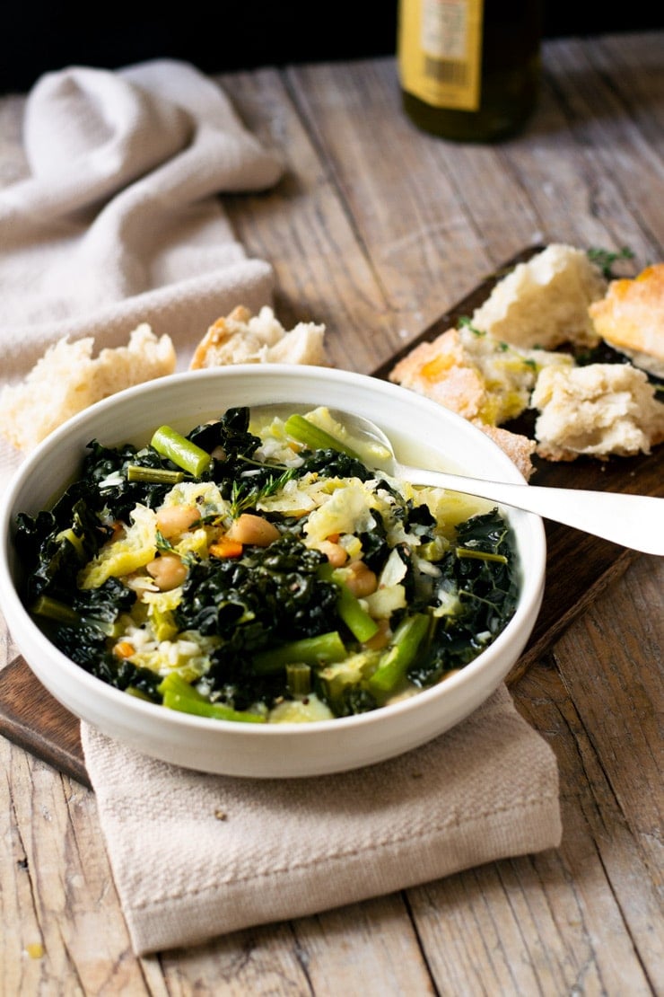 A bowl of Tuscan minestrone soup on a wooden surface with bread