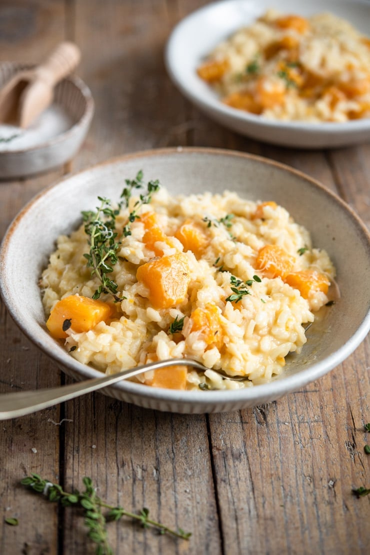 A side shot of butternut squash risotto in a rustic bowl topped with fresh thyme