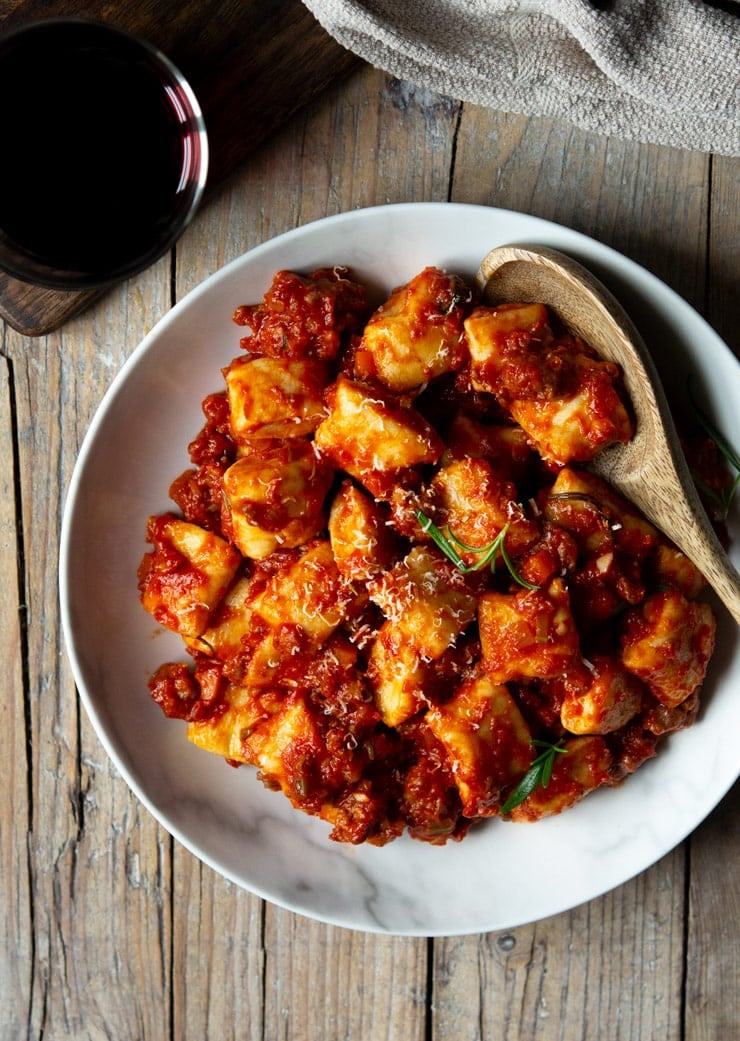 An overhead shot of sausage ragu tossed with ricotta gnocchi in a large white bowl