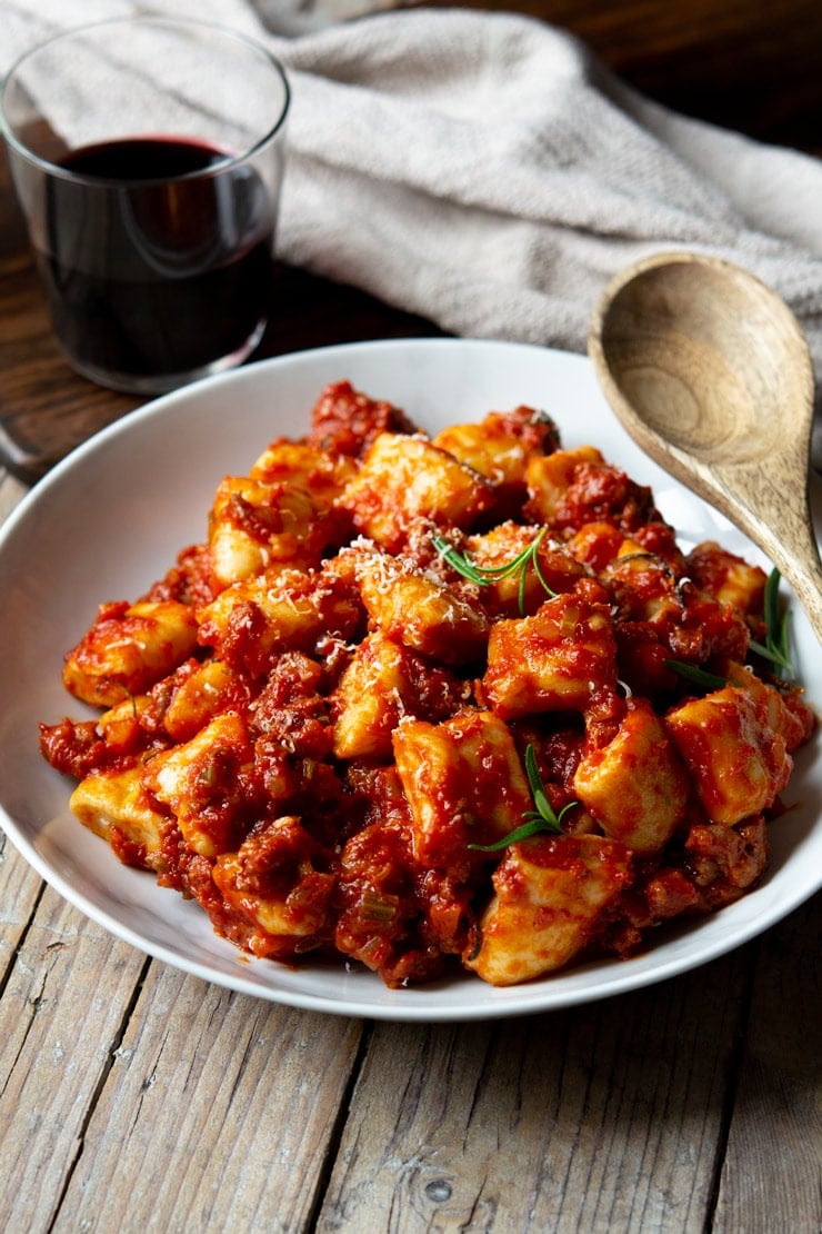 Sausage ragu in a bowl with ricotta gnocchi and a glass of red wine in the background