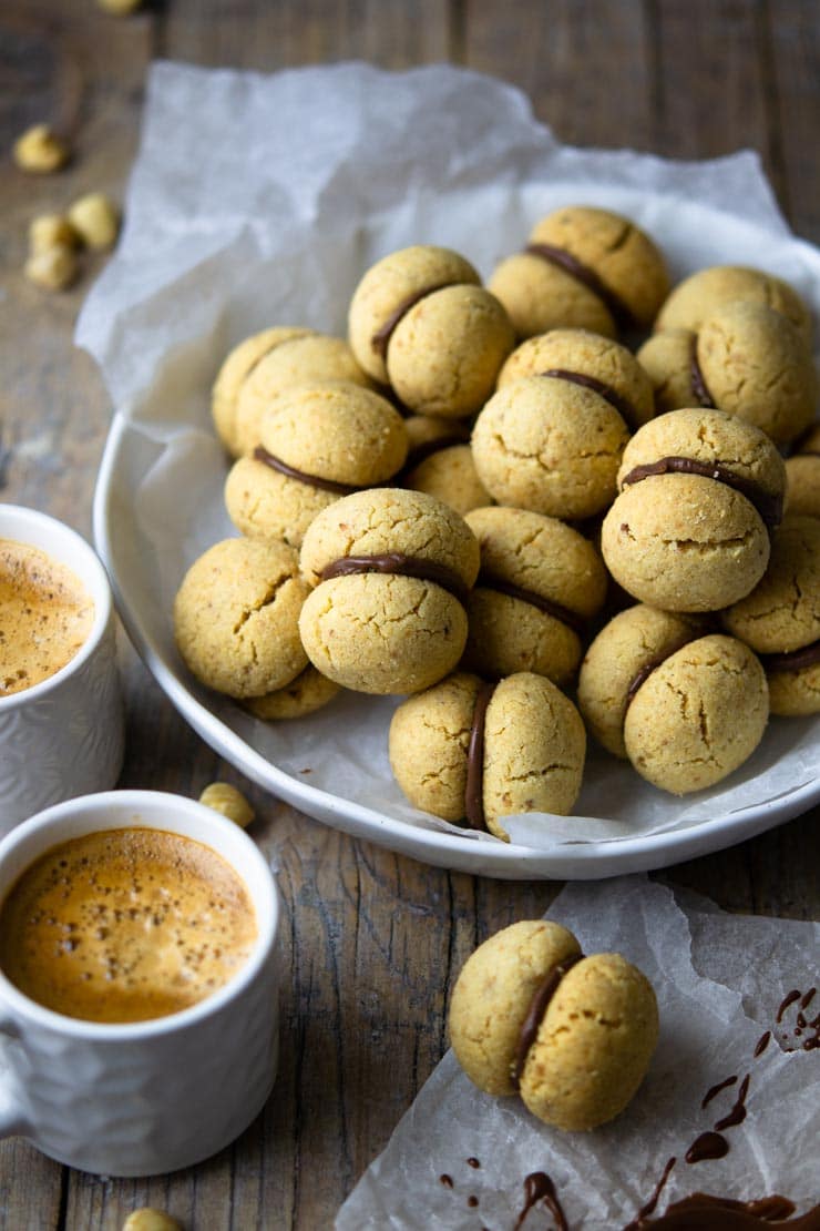 A close up of lady's kisses cookies in a bowl with two cups of coffee at the side