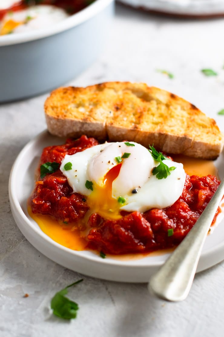 A close up of eggs in purgatory on a plate with a runny egg yolk