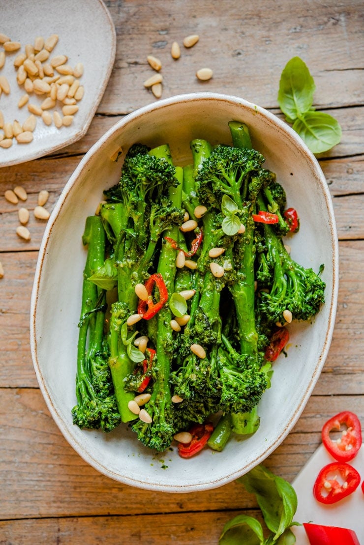 An overhead shot of sauteed broccolini in a serving bowl with pine nuts on top