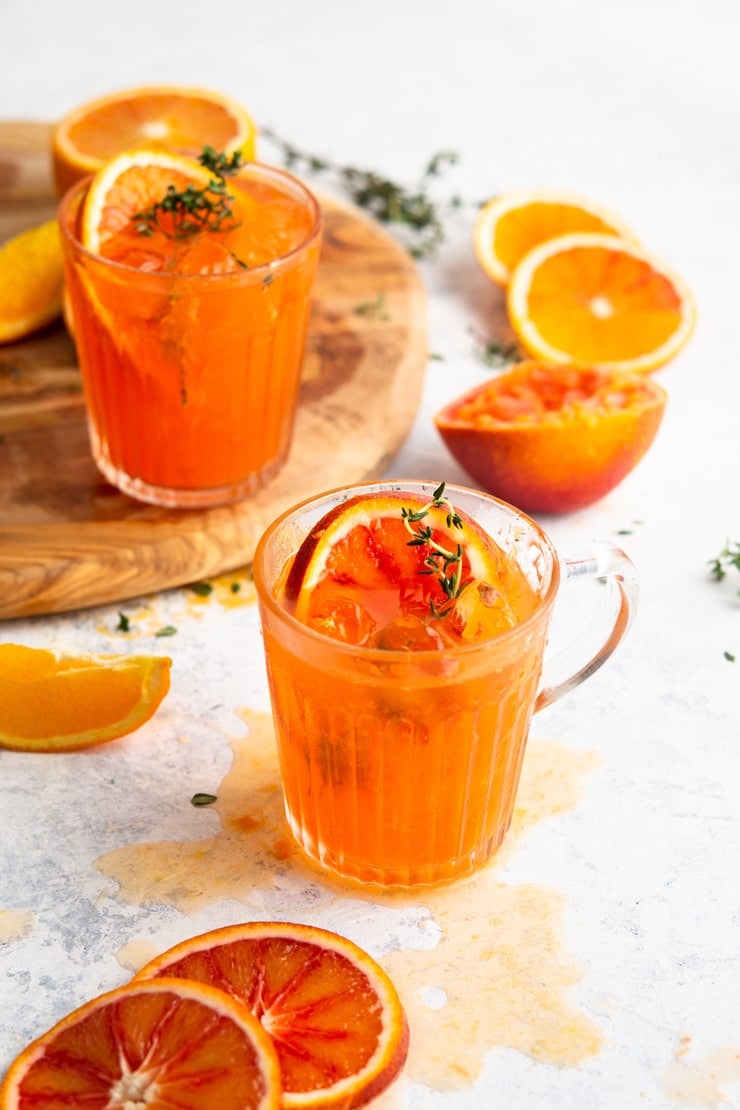 A blood orange cocktail in a glass with slices of orange all around and sprigs of thyme
