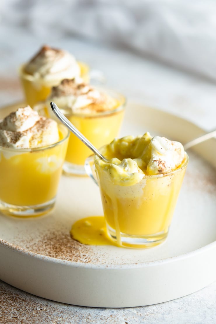 A close up of an espresso cup filled with bombardino eggnog liqueur and spilling over the edge