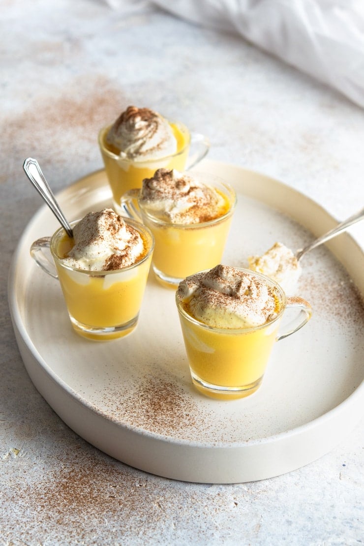 Four glasses of Bombardino drinks on a white plate with whipped cream and cinnamon