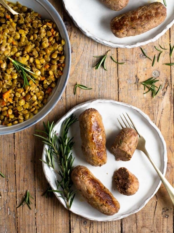 Homemade sausages on a plate next to a bowl of green lentils