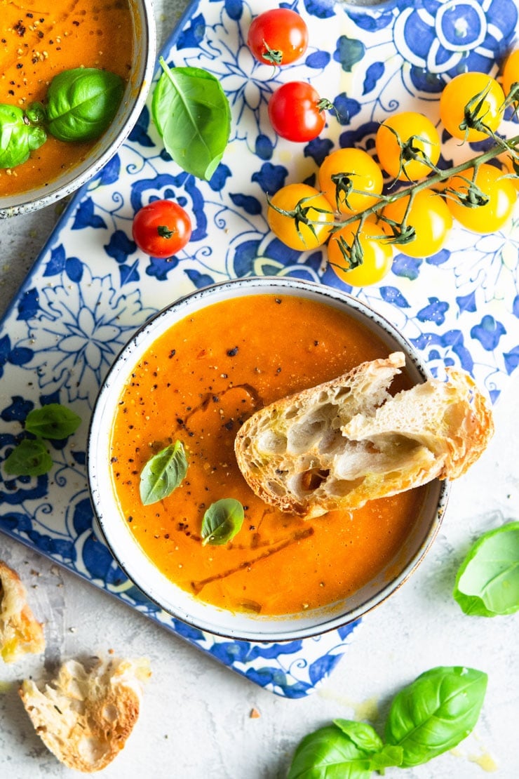 An overhead shot of roasted tomato soup in a bowl with basil and vine tomatoes at the side