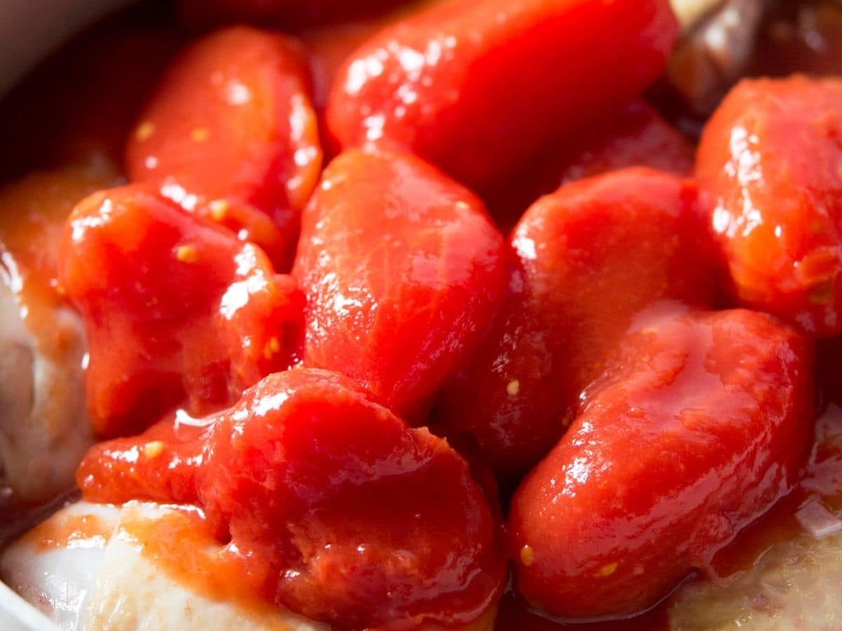 A close up of canned plum tomatoes in a pot with chicken.