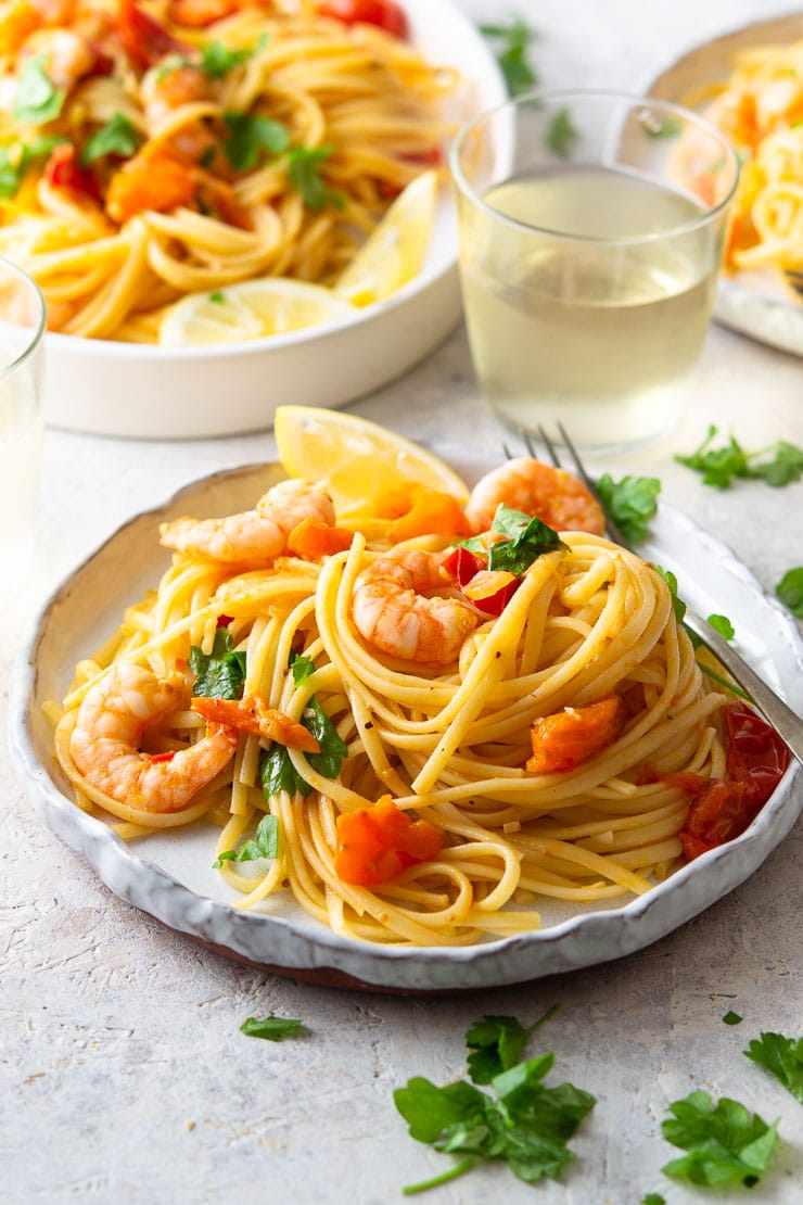 A close up of shrimp linguine on a plate with parsley and lemon