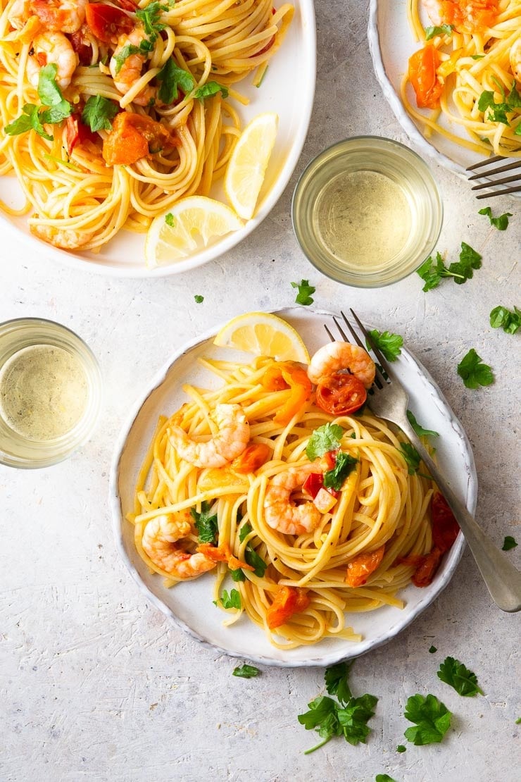 An overhead shot of shrimp linguine on a plate with glasses of white wine, parsley and lemon