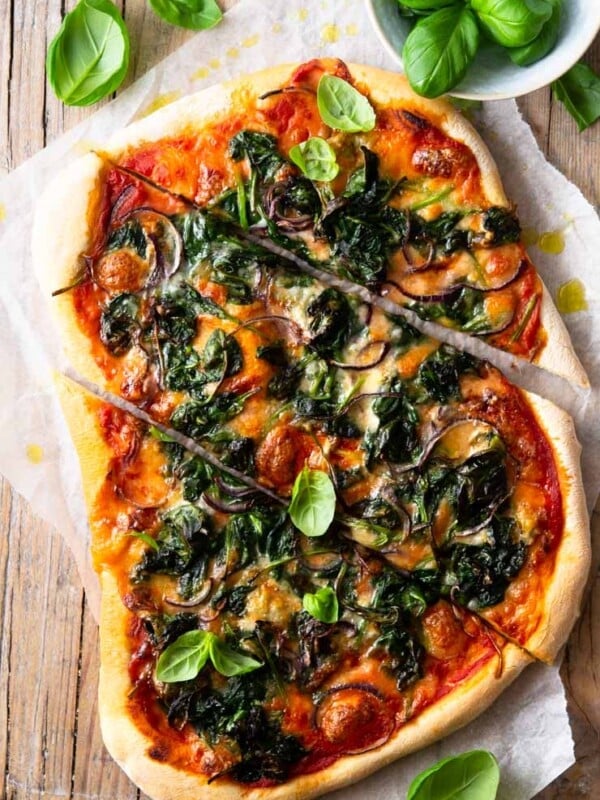 A spinach pizza on a wooden surface cut into slices