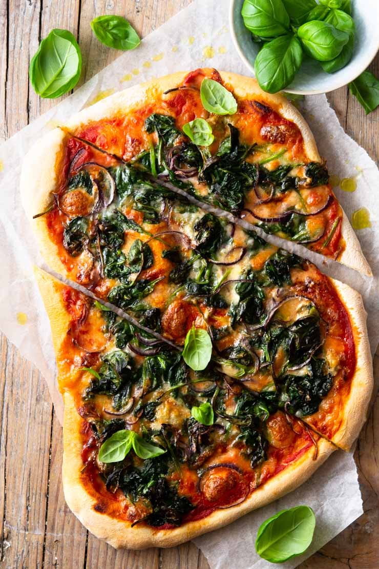 A spinach pizza on a wooden surface cut into slices