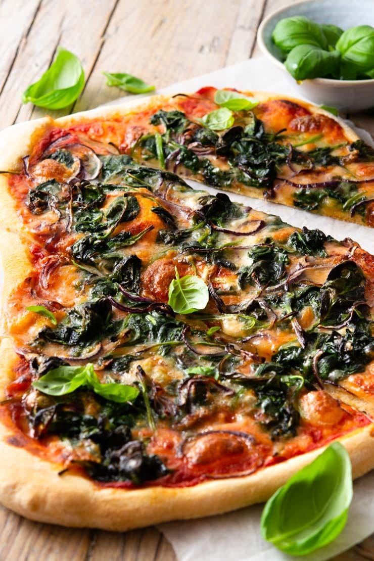 A close up of a spinach pizza cut into slices with gorgonzola cheese and red onion