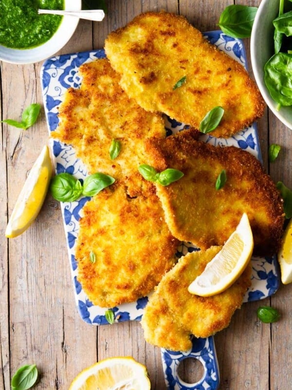 Italian chicken cutlets on a board with lemon wedges