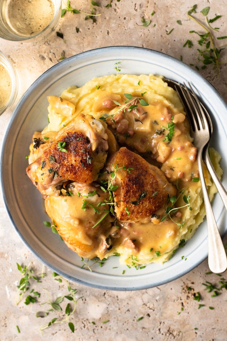 An overhead shot of creamy Tuscan chicken with mashed potatoes in a blue bowl