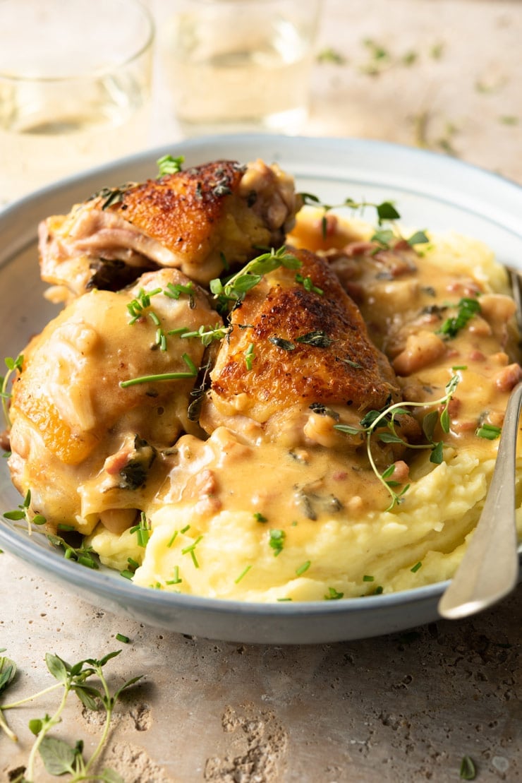 A side shot of creamy Tuscan chicken in a blue bowl with mashed potatoes