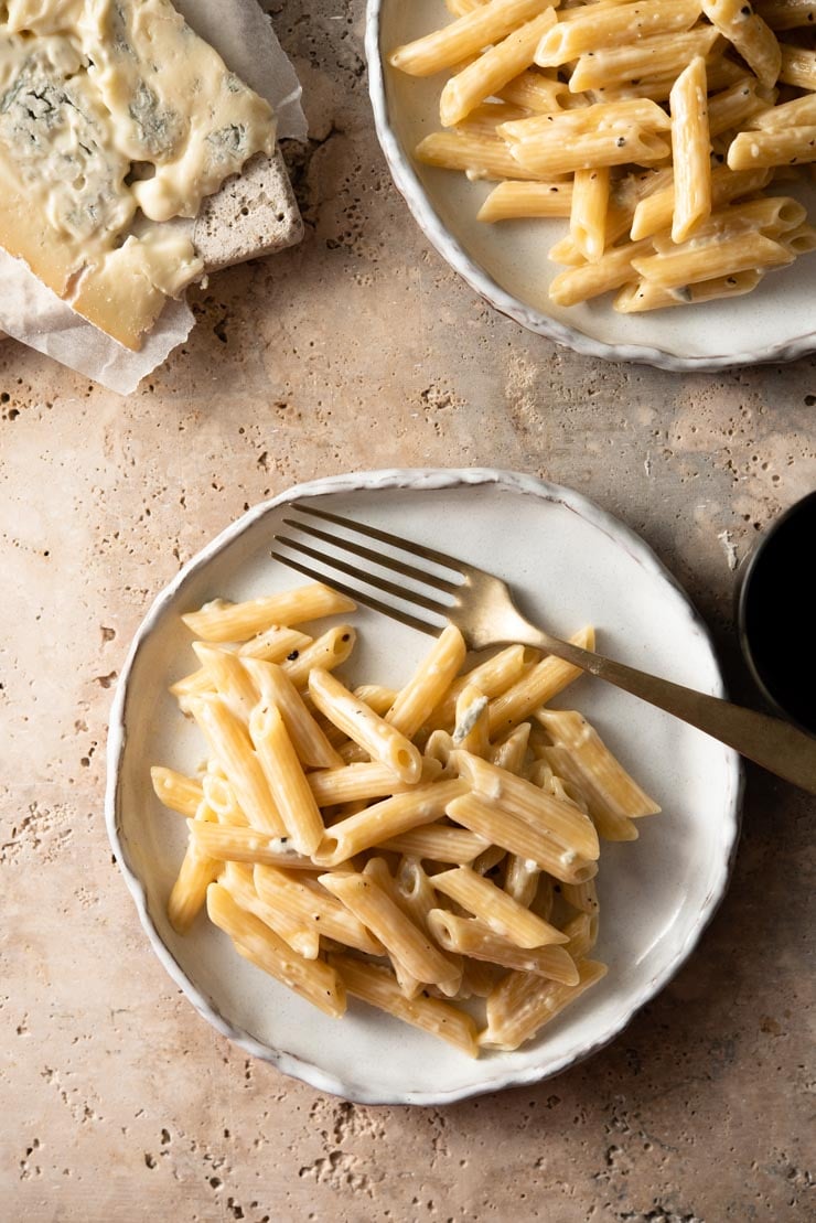 An overhead shot of plates of pasta with gorgonzola sauce and a block of melting gorgonzola in the background