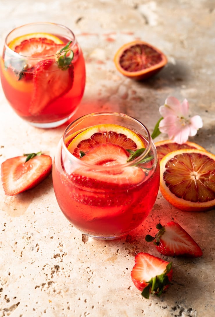 A campari cocktail in two round glasses garnished with fruit