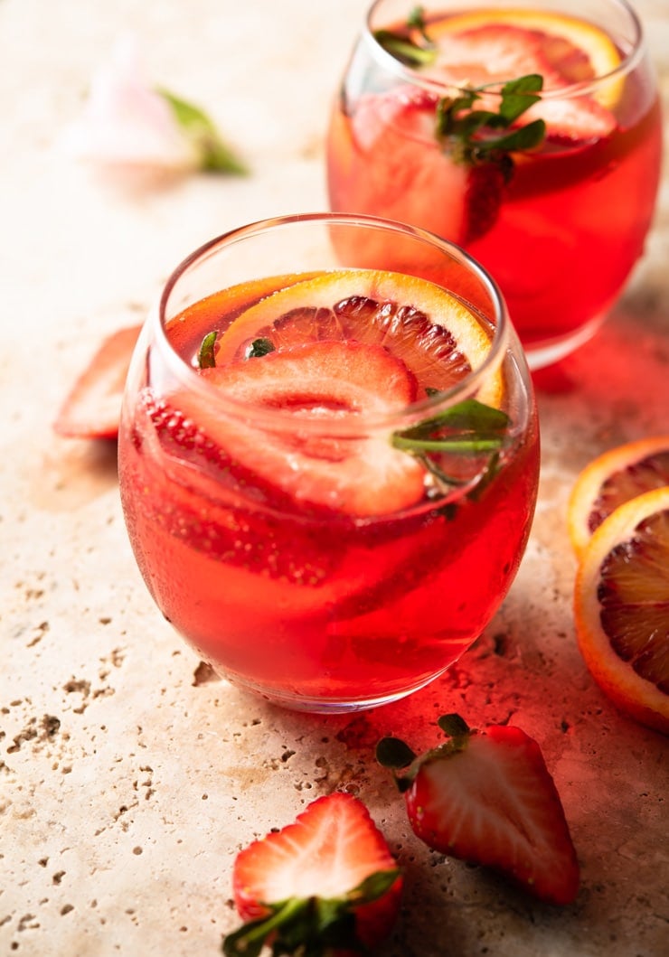 A close up of a campari spritz in a glass with fresh strawberries and oranges