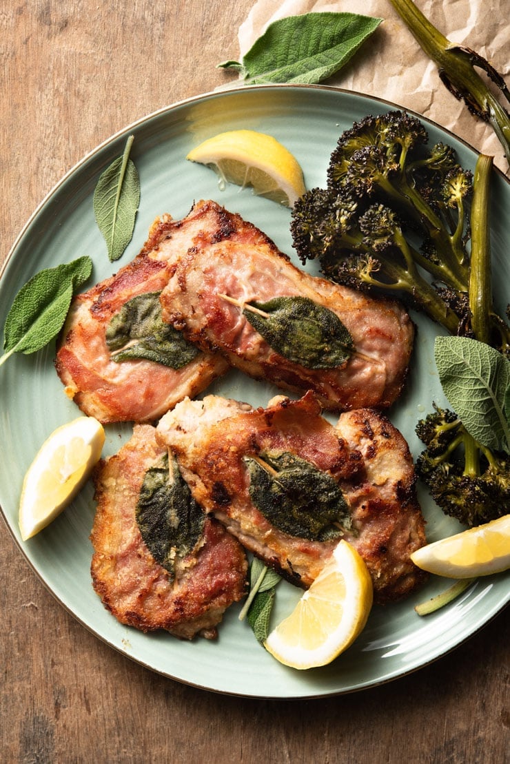 An overhead shot of veal saltimbocca on a plate with prosciutto, sage and lemon wedges