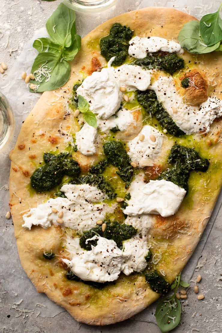 An overhead shot of a cheesy basil pizza with pesto and burrata