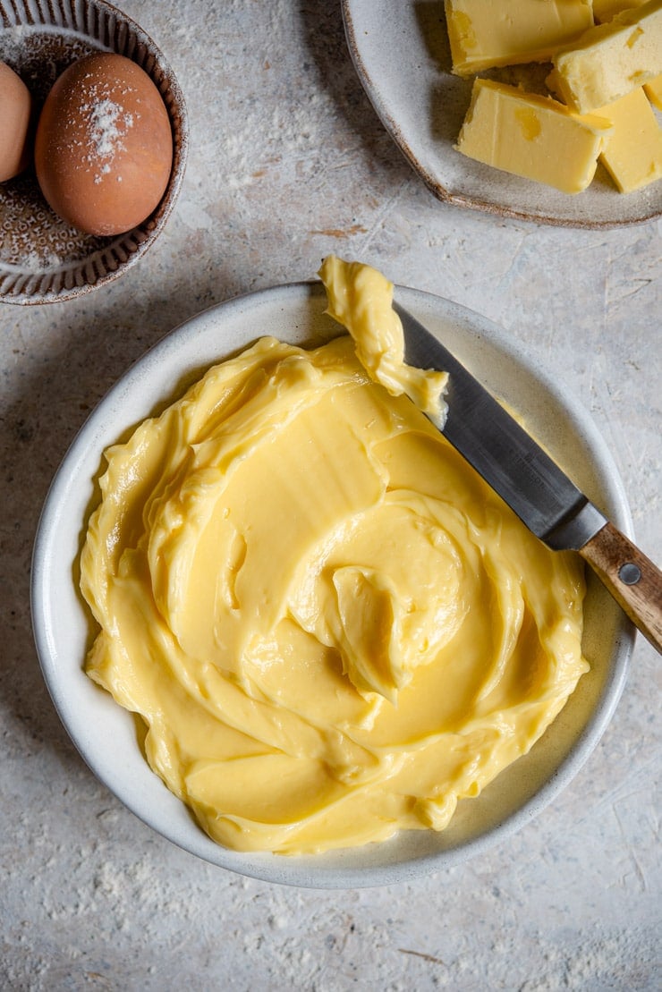 How to soften butter using the easiest method ever! If your doing some baking and need soft, creamy butter asap then this method is for you and there's not a microwave in sight! It takes only 5 minutes and works every single time without any risk of your butter melting. #cookingtips An overhead shot of softened butter in a rustic bowl