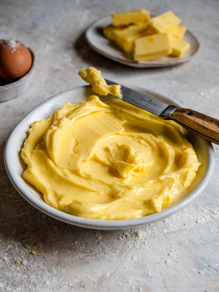 A side shot of softened butter in a bowl with a knife