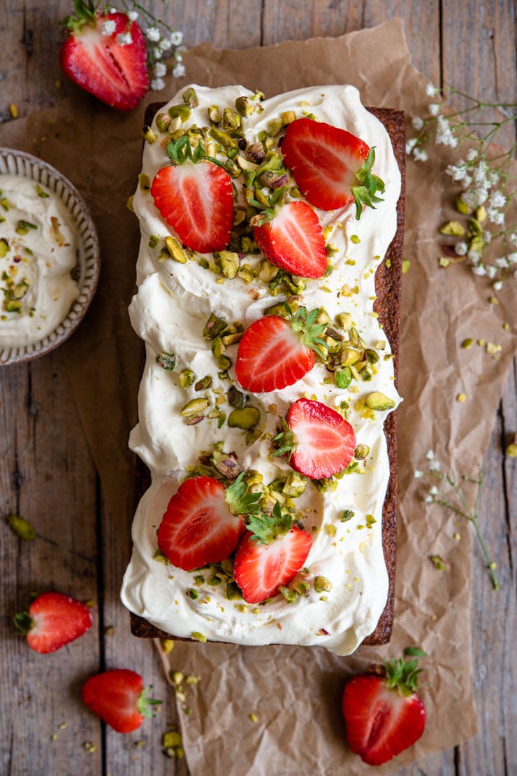 An overhead shot of a pistachio cake topped with whipped cream and fresh strawberries