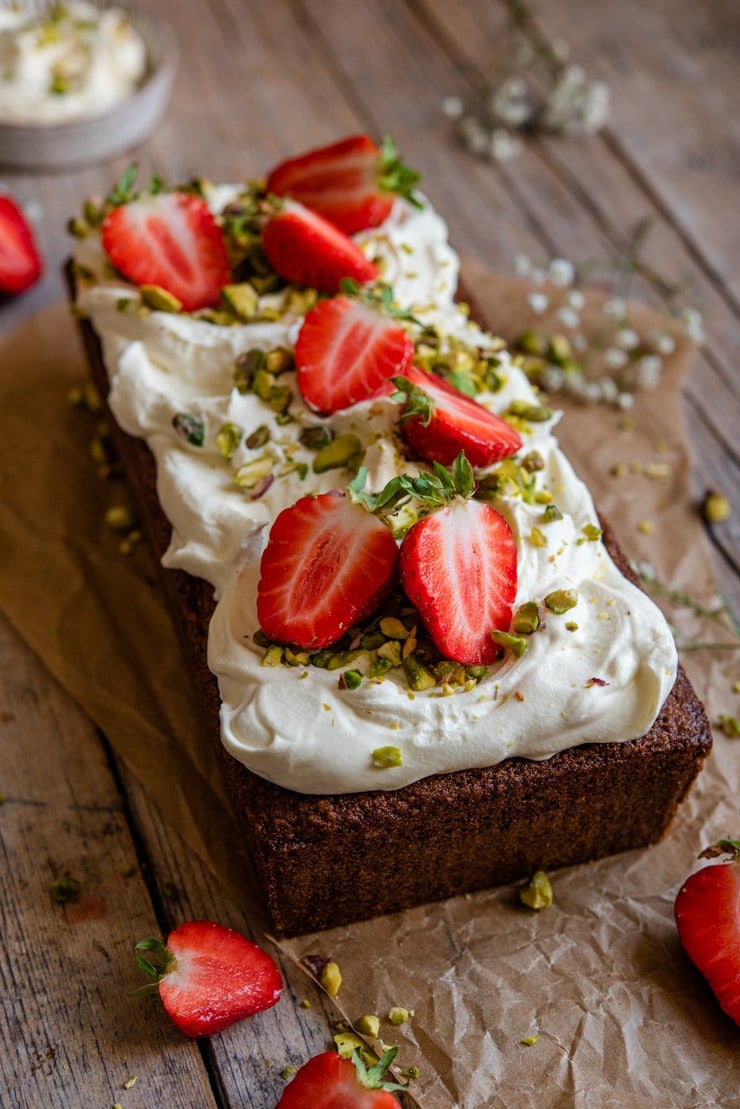 A side shot of a pistachio cake topped with whipped cream and strawberries