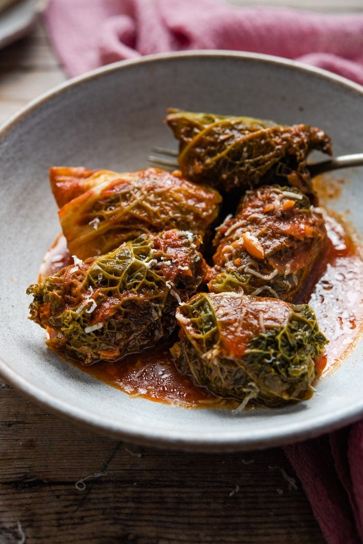 A close up of Italian stuffed cabbage rolls in a rustic bowl with tomato sauce