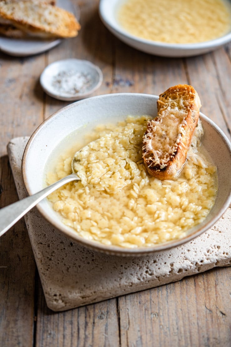 A close up of pastina soup with crusty bread at the side