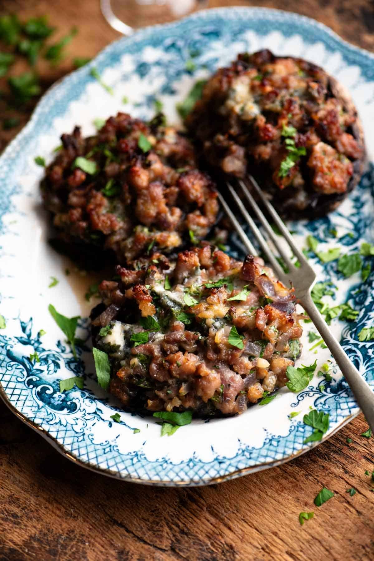 A white and blue patterned plate with 3 large mushrooms stuffed with sausage and gorgonzola.