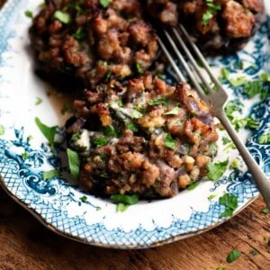 A close up of a portobello msuhroom stuffed with sausage and gorgonzola on a blue and white plate.