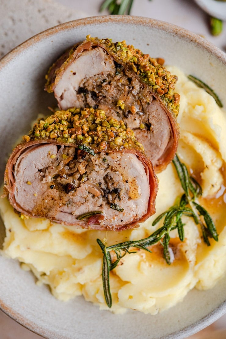 A close up of stuffed pork tenderloin sitting on top of mashed potatoes