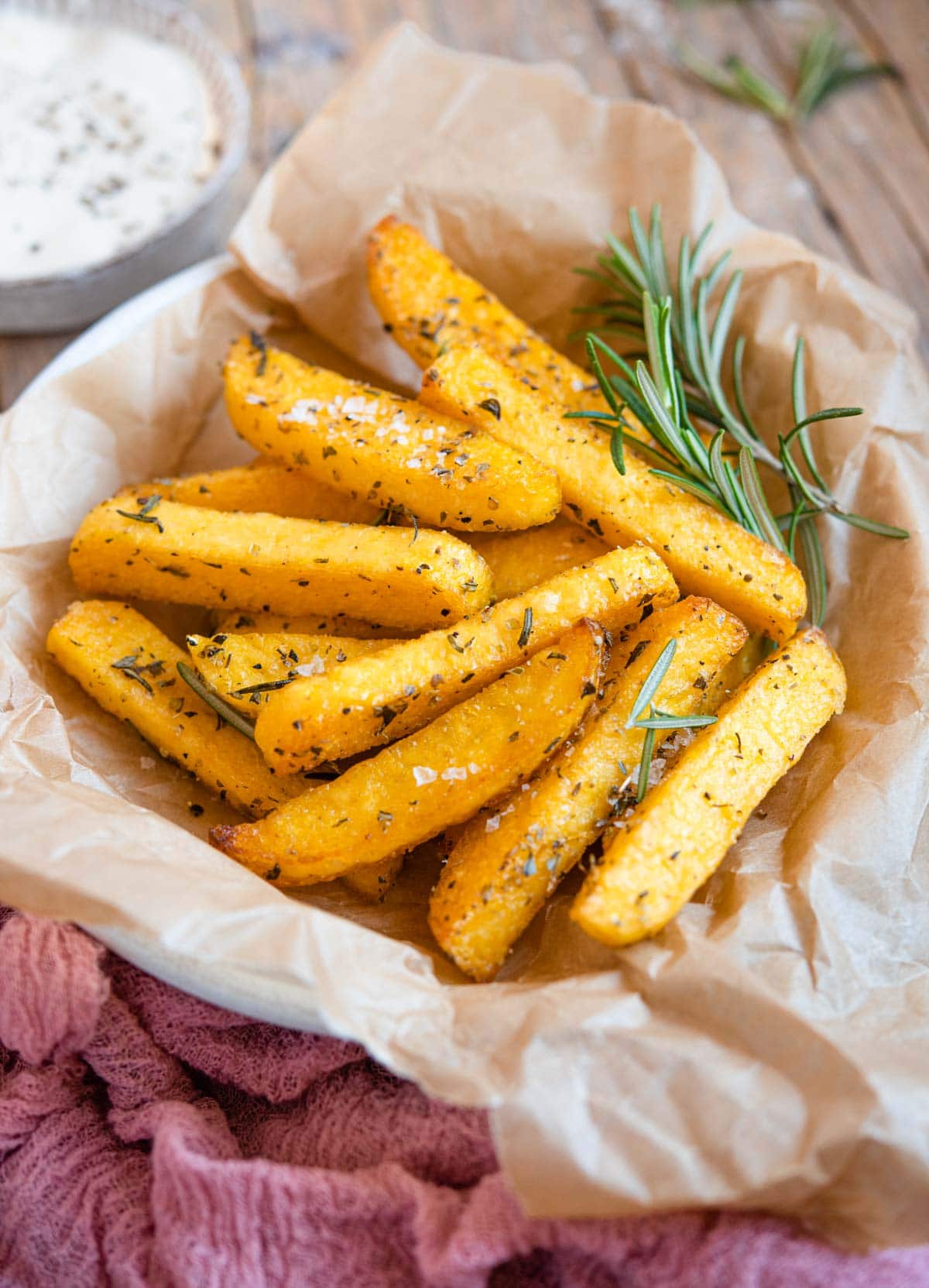 A side shot of polenta fries in a bowl with rosemary