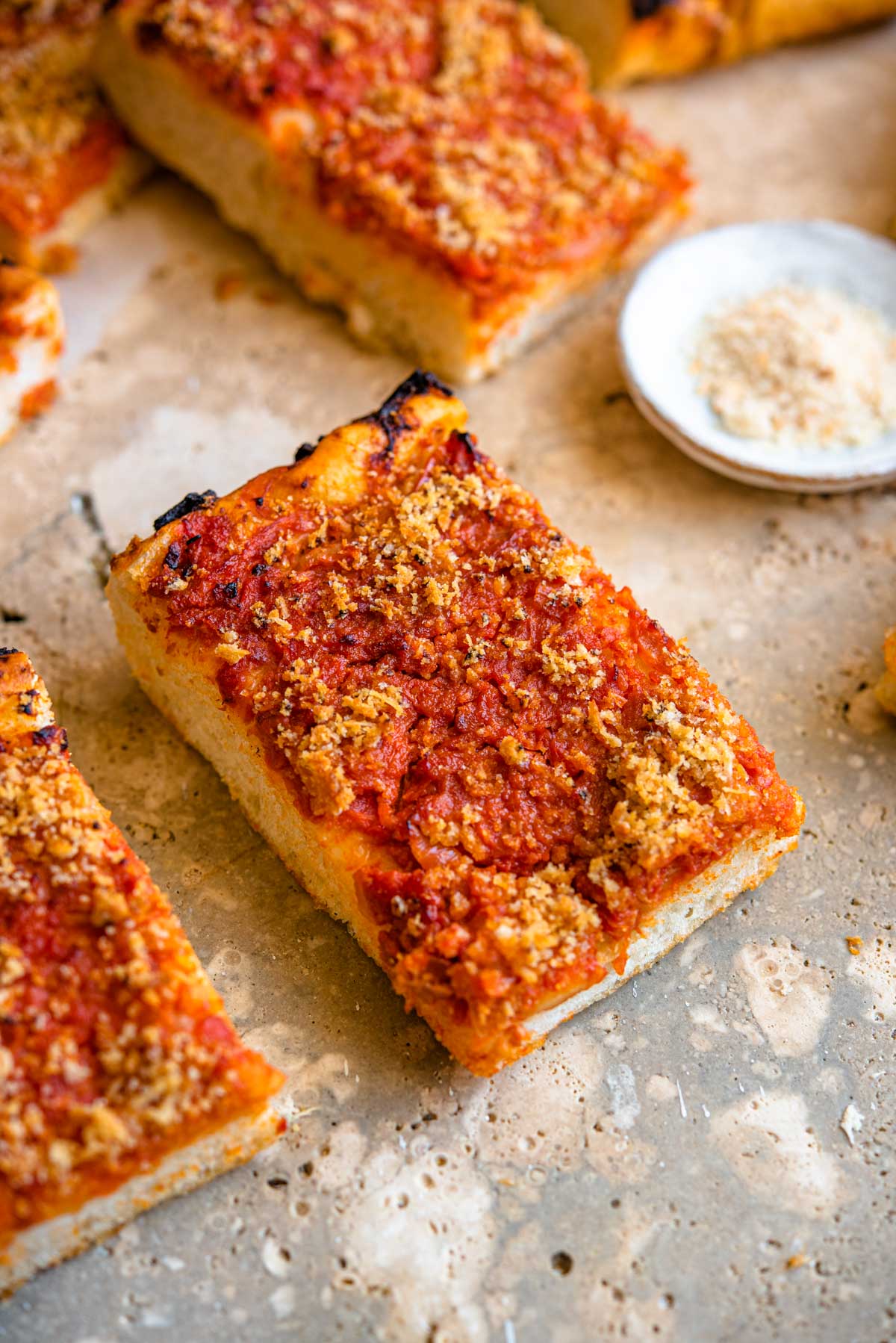 A close up of a slice of Sicilian pizza with breadcrumbs at the side