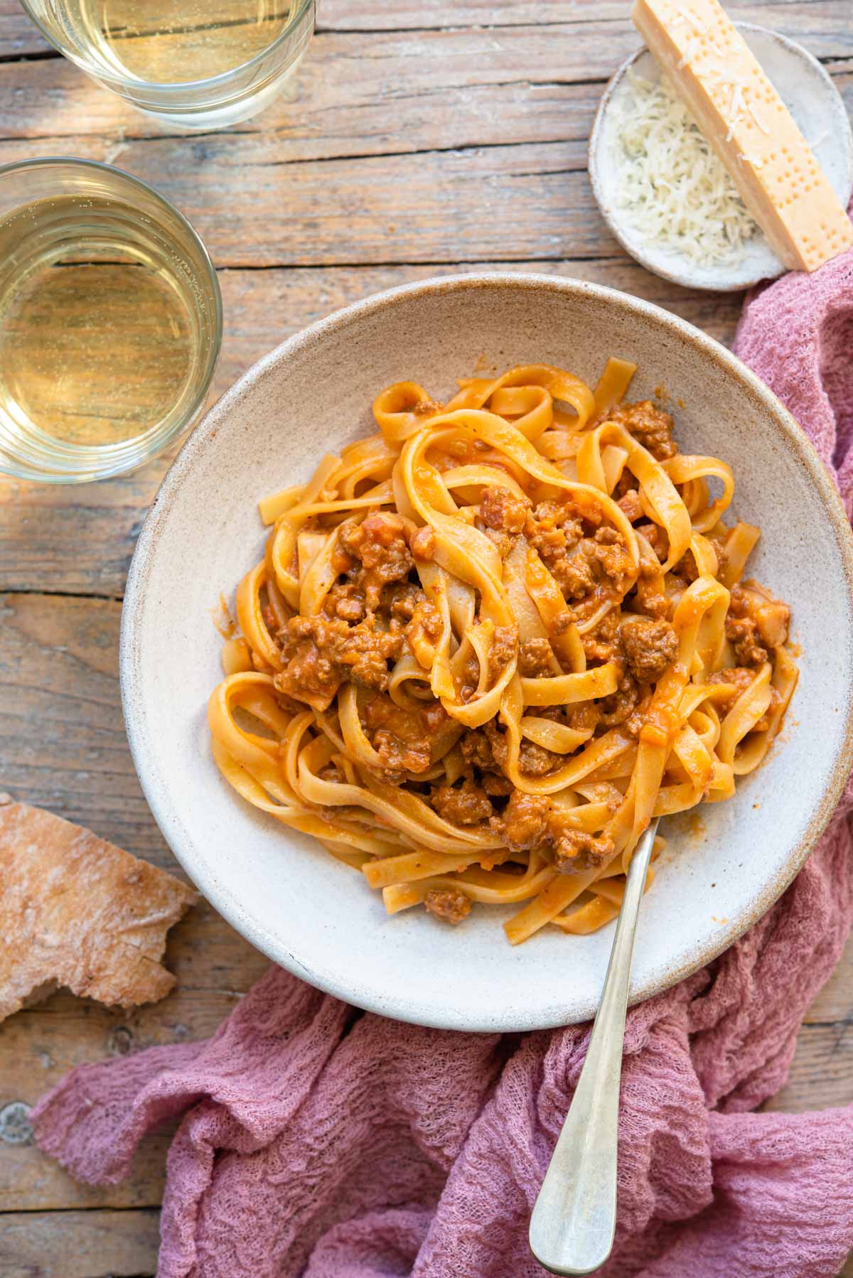 An overhead shot of tagliatelle with bolognese sauce in a bowl with a glass of wine beside it