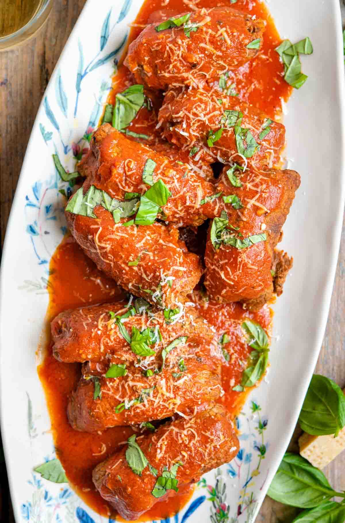 An overhead shot of braciole on a serving platter covered in tomato sauce