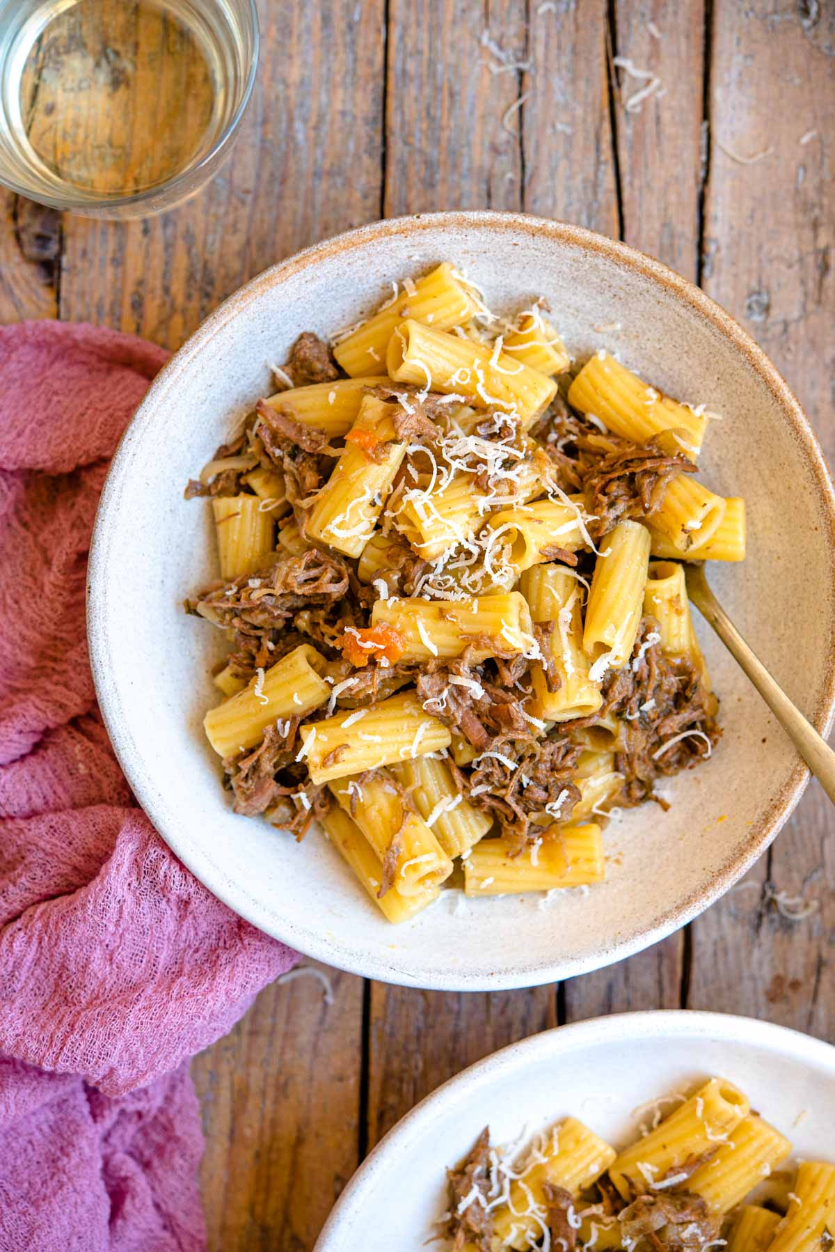 An overhead shot of Genovese sauce with rigatoni pasta in a bowl with a glass of wine beside it