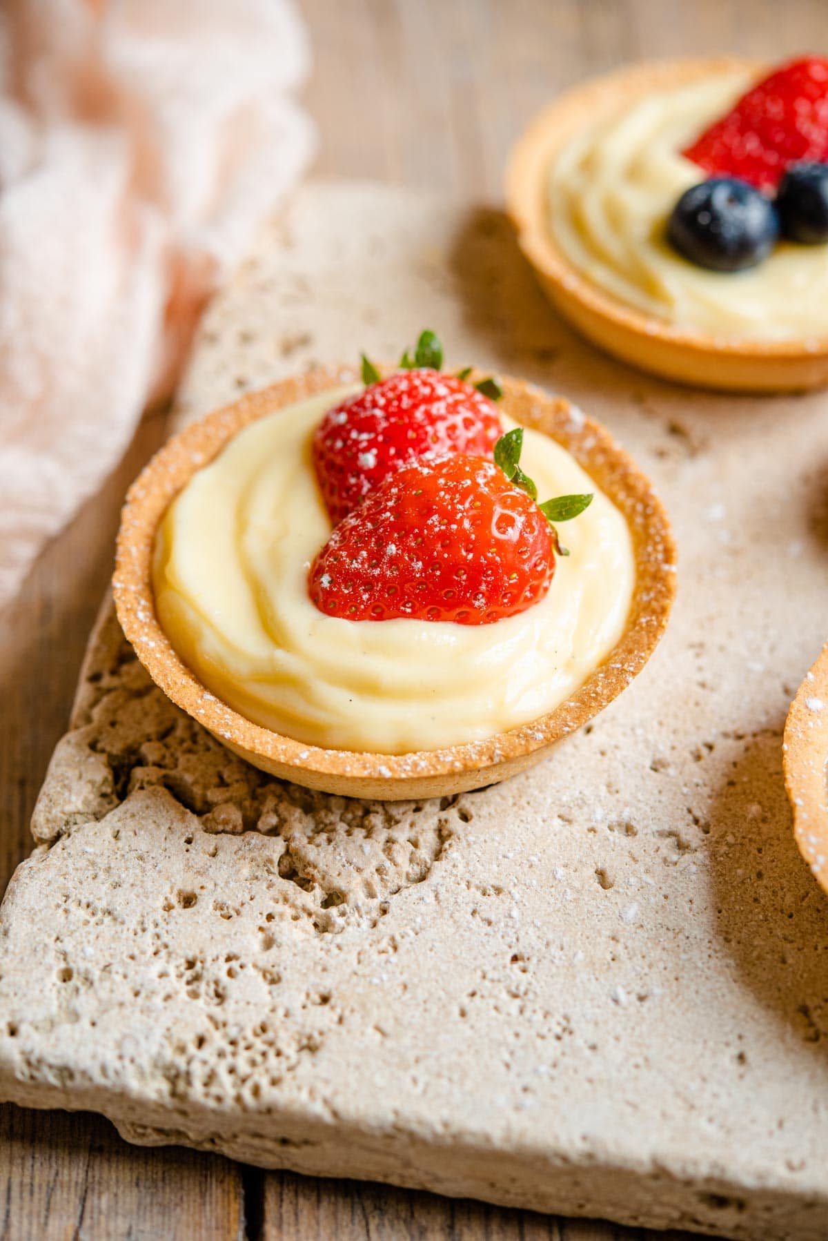 A small individual sized pie crust filled with Italian pastry cream and topped with two slices of strawberry.