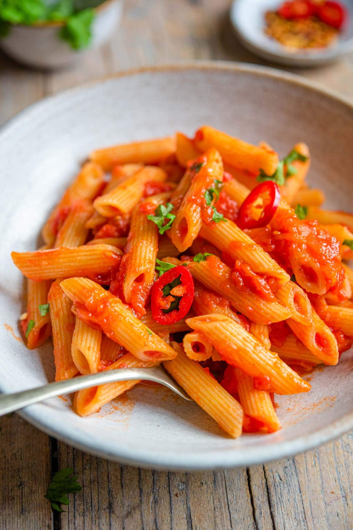 A close up of penne arrabbiata in a rustic bowl with a fork