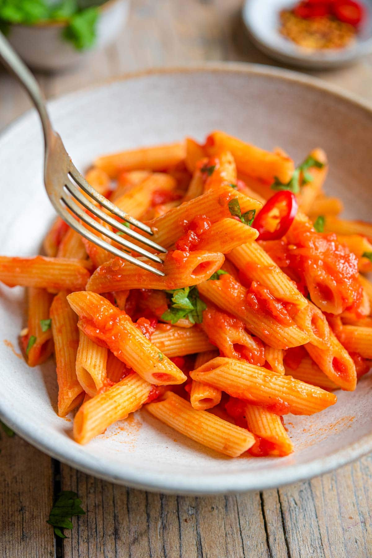 A close up of a fork picking up penne pasta from a bowl