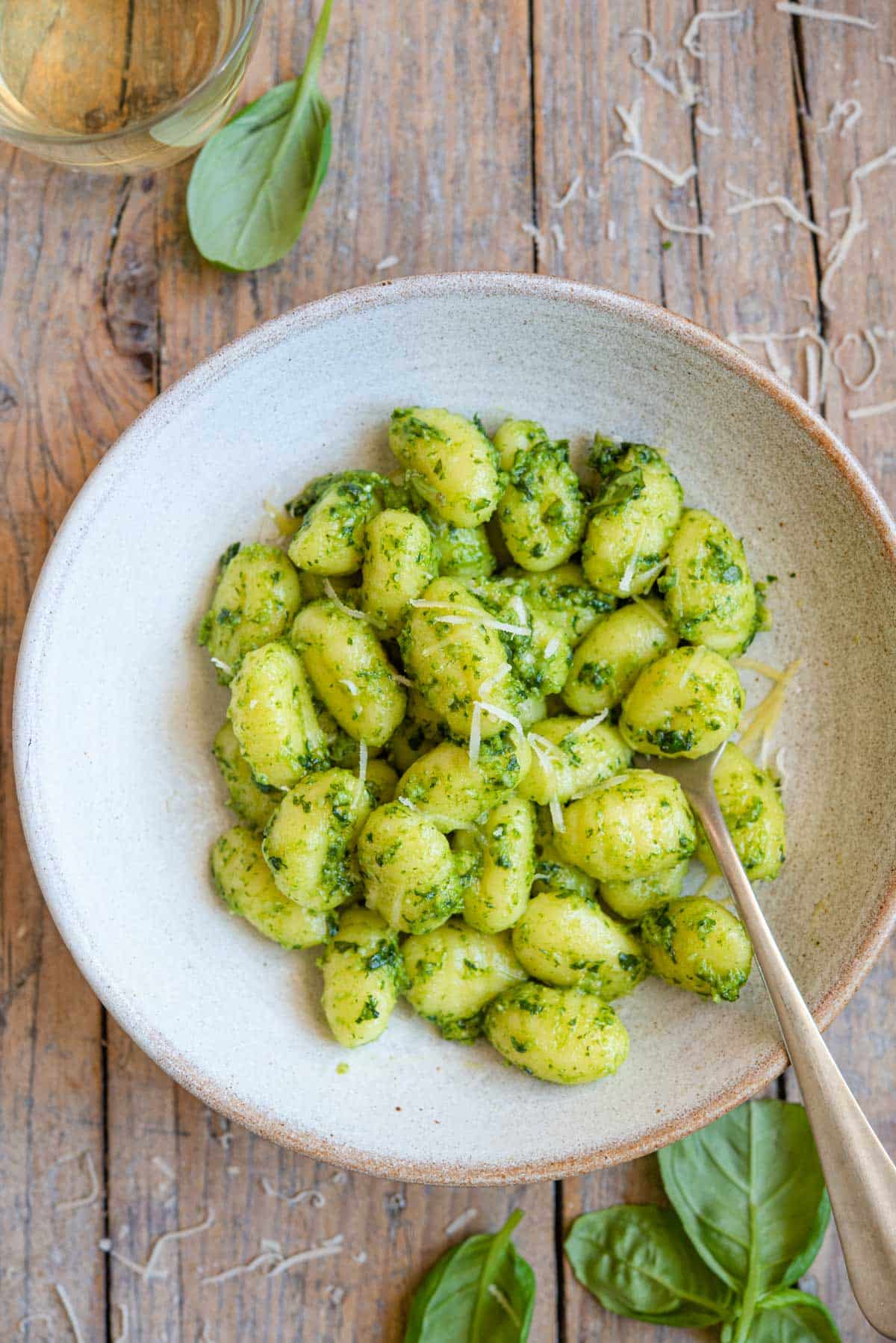 An overhead shot of pesto gnocchi in a rustic bowl sitting on a wooden surface