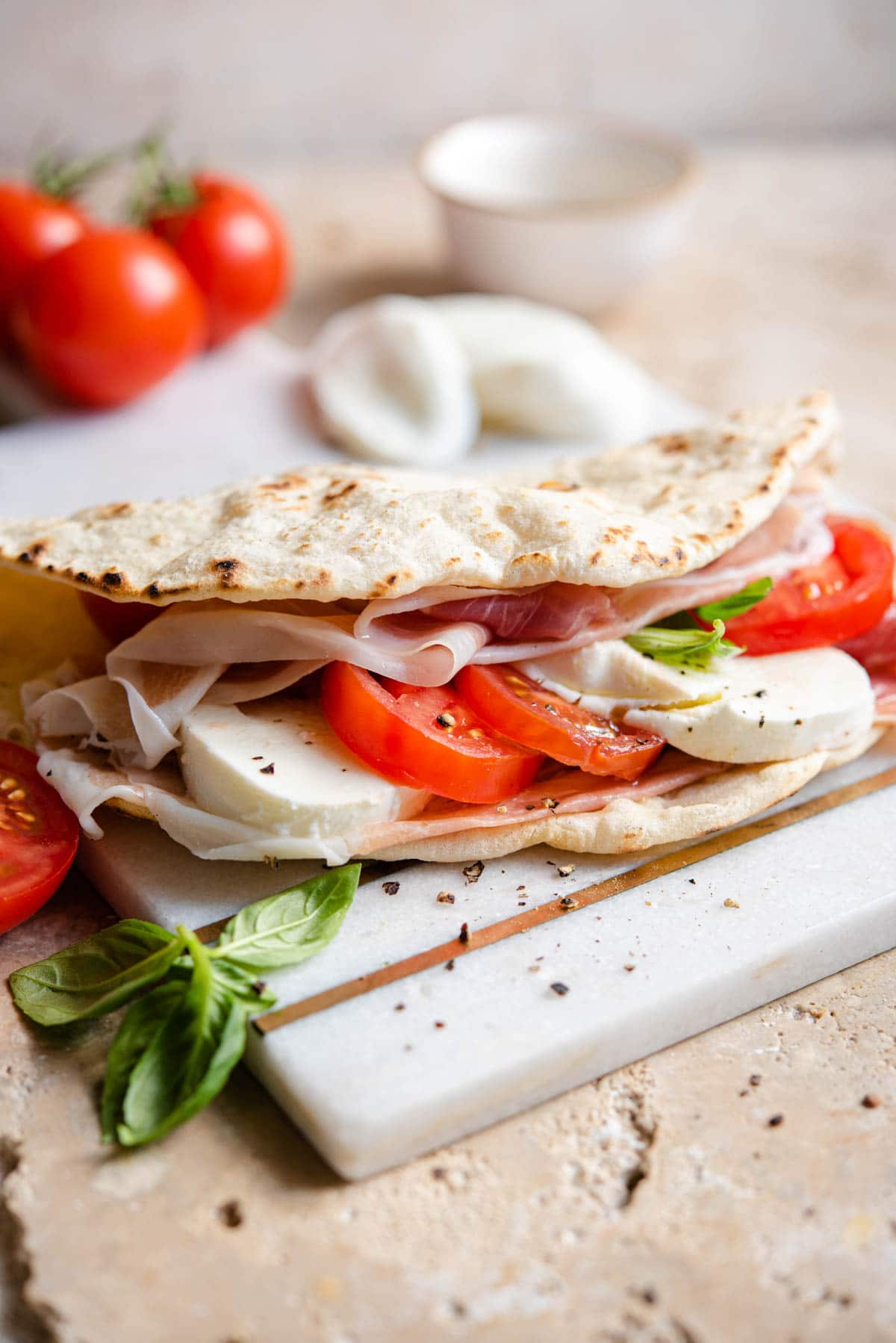 A Piadina flatbread stiffed with tomato, mozzarella and prosciutto on a marble board