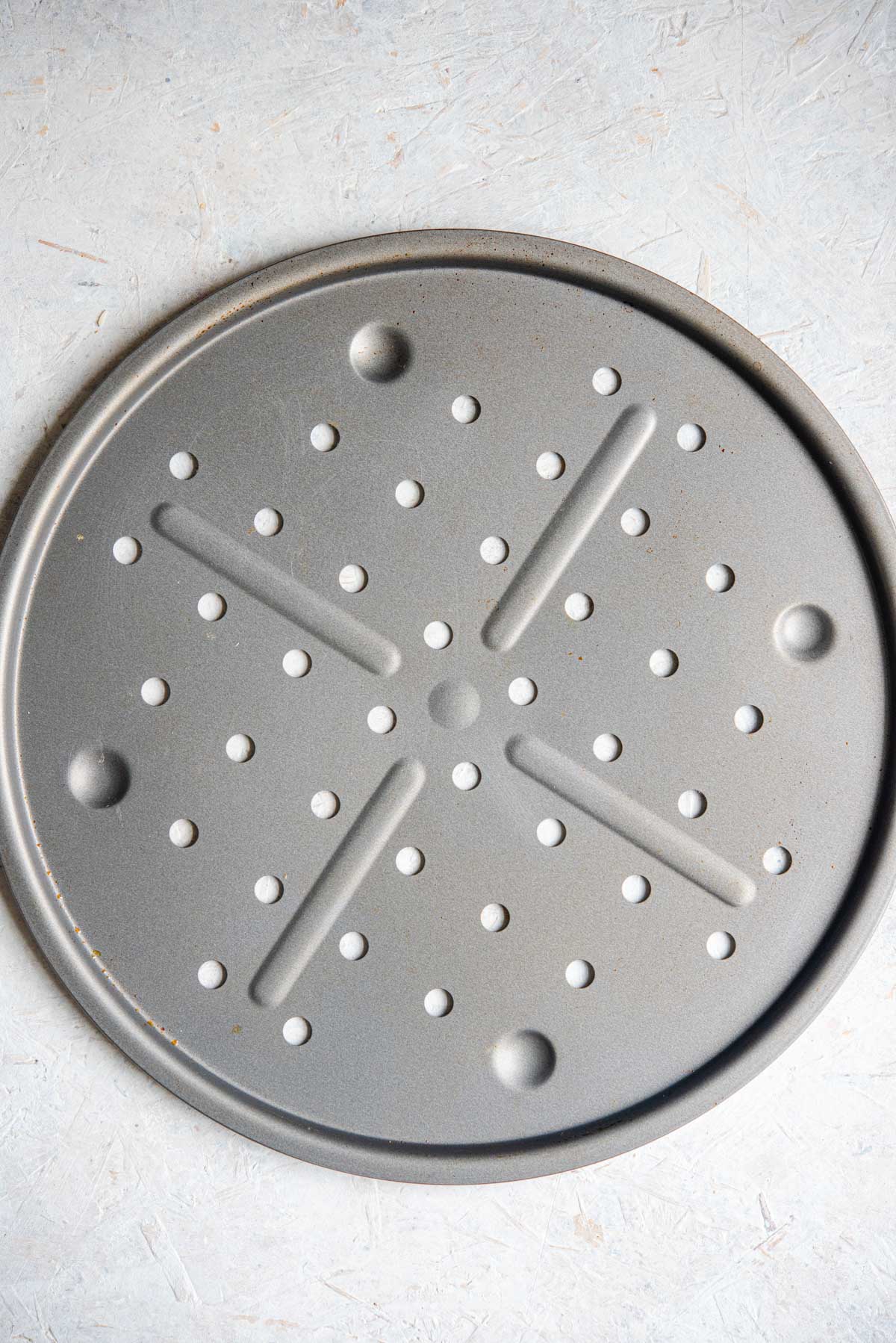 An overhead shot of a circular pizza tray with holes