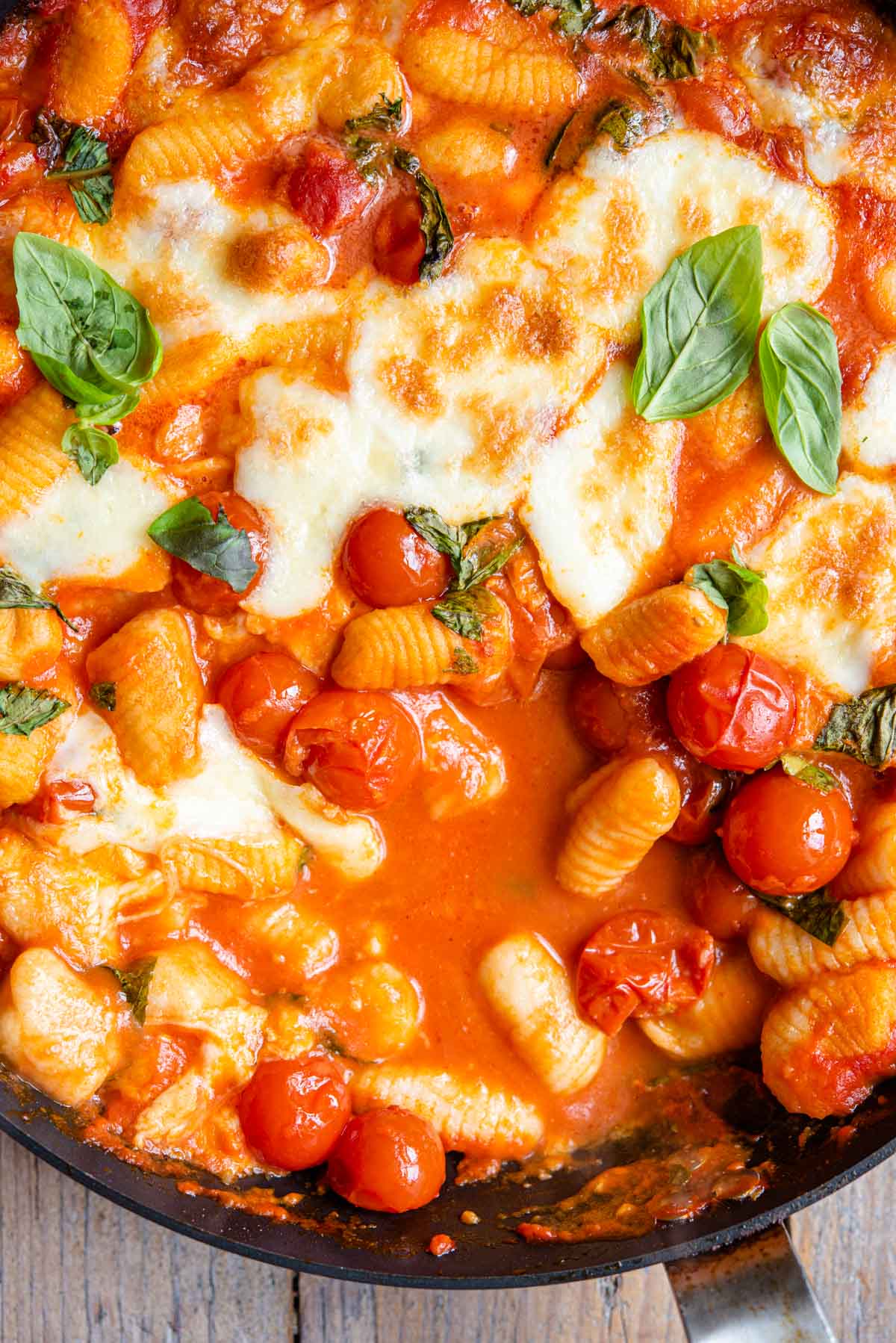 A close up of gnocchi in a skillet with a tomato sauce, mozzarella and basil