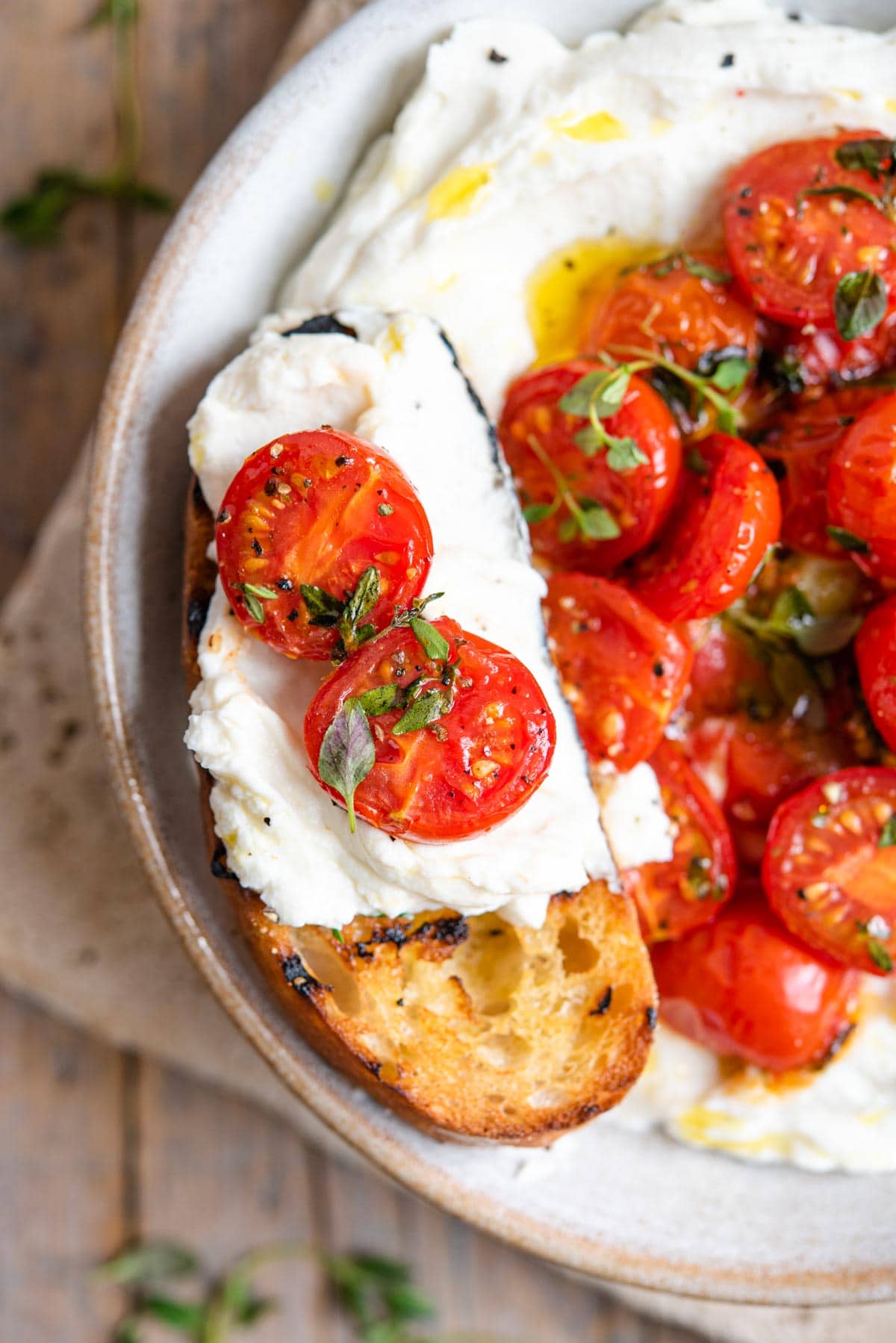 A close up of a slice of ciabatta bread topped with whipped ricotta and tomatoes