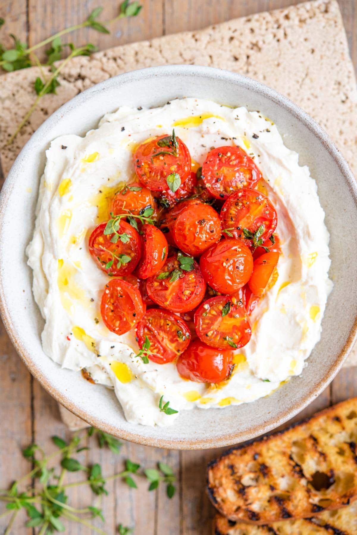 An overhead shot of ricotta in a serving bowl topped with roasted tomatoes