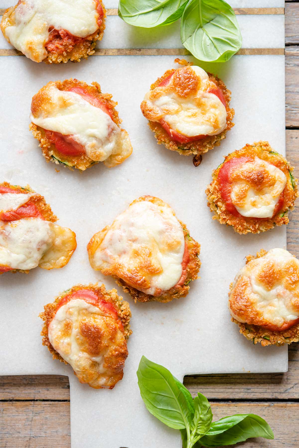 An overhead shot of zucchini pizza bites on a marble cutting board
